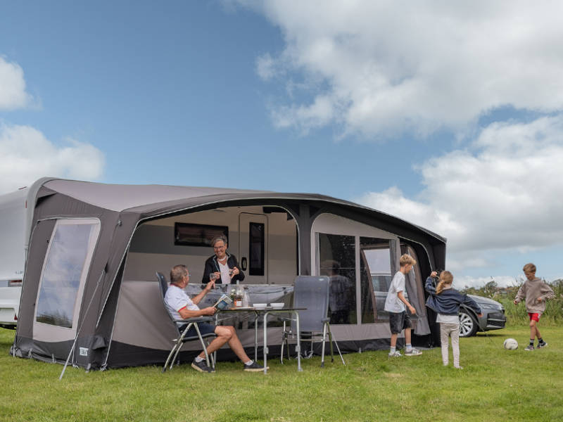 Family enjoying a picnic under a caravan awning on a sunny day.