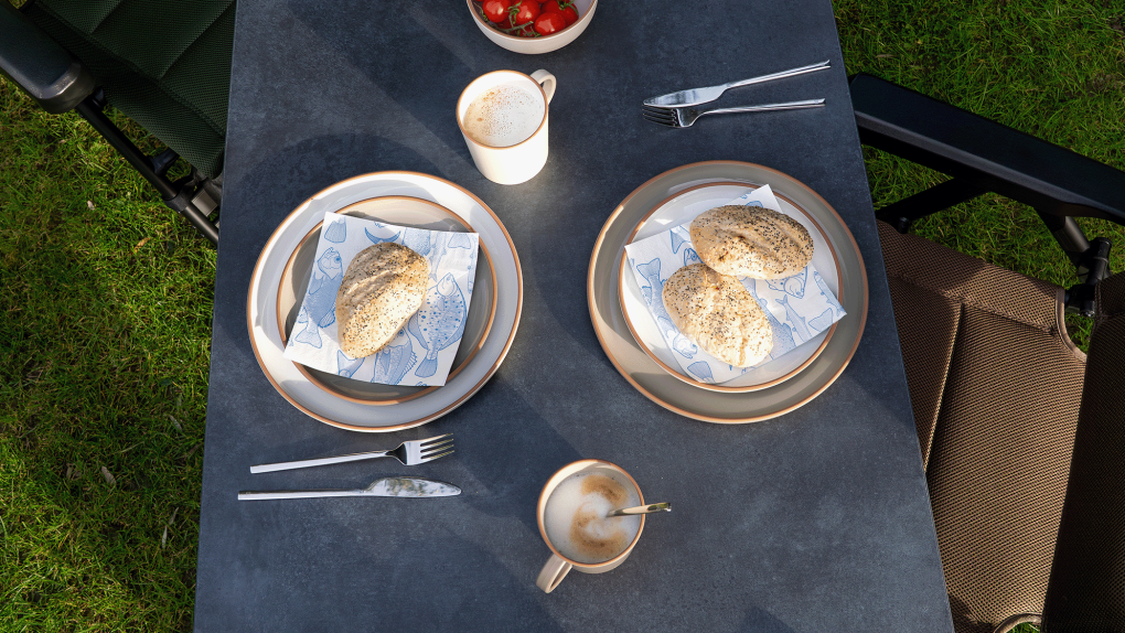 Outdoor setting with plates of food on a tablecloth, surrounded by grass.