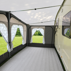 Caravan with an attached awning and curtains, set against a grassy outdoor background.