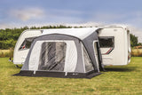 Caravan with a gray and black inflatable awning on a grassy area.