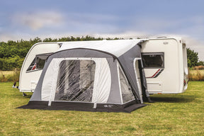 Caravan with a gray and black inflatable awning on a grassy area.