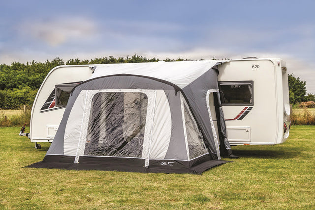 Caravan with a gray and black inflatable awning on a grassy area.