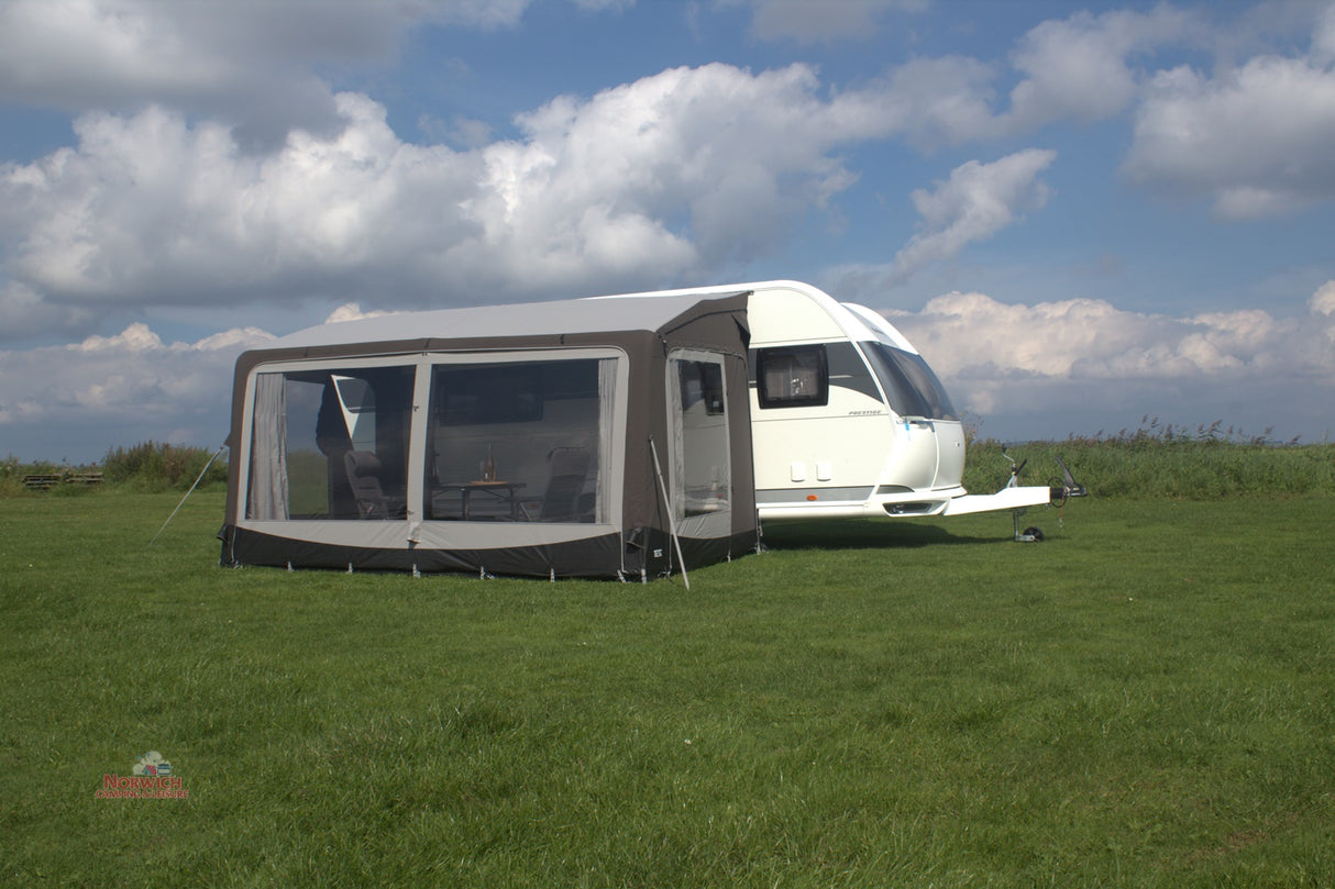 Caravan with an awning on a grassy field under a blue sky with clouds