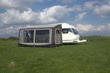 Caravan with an awning on a grassy field under a blue sky with clouds