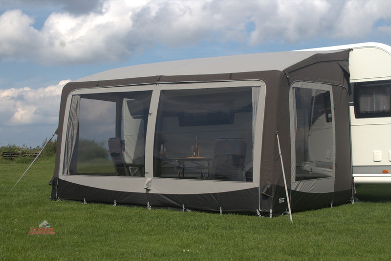 Caravan with a screen porch on a grassy area under a cloudy sky