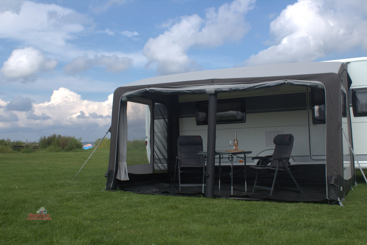 Caravan with an awning extended on a grassy area under a blue sky with clouds.
