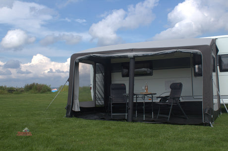 Caravan with an awning extended on a grassy area under a blue sky with clouds.